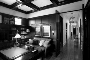 Black and white image of an office with leather furniture and wood decorated walls.